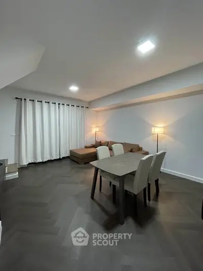 Modern living room with elegant dining area and cozy lighting, featuring sleek hardwood floors and contemporary furniture.