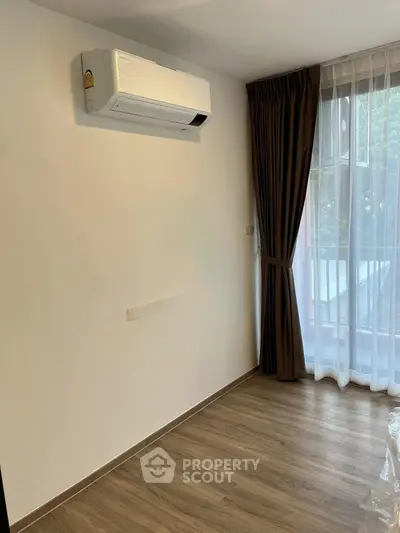 Modern room with air conditioning and large window with curtains, featuring wooden flooring.