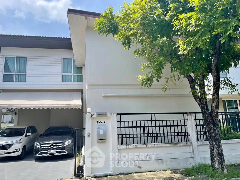 Charming two-story house with carport and lush tree-lined street view.