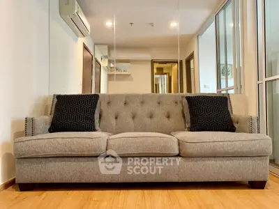 Modern living room with stylish gray sofa and decorative pillows, featuring mirrored wall and wooden flooring.