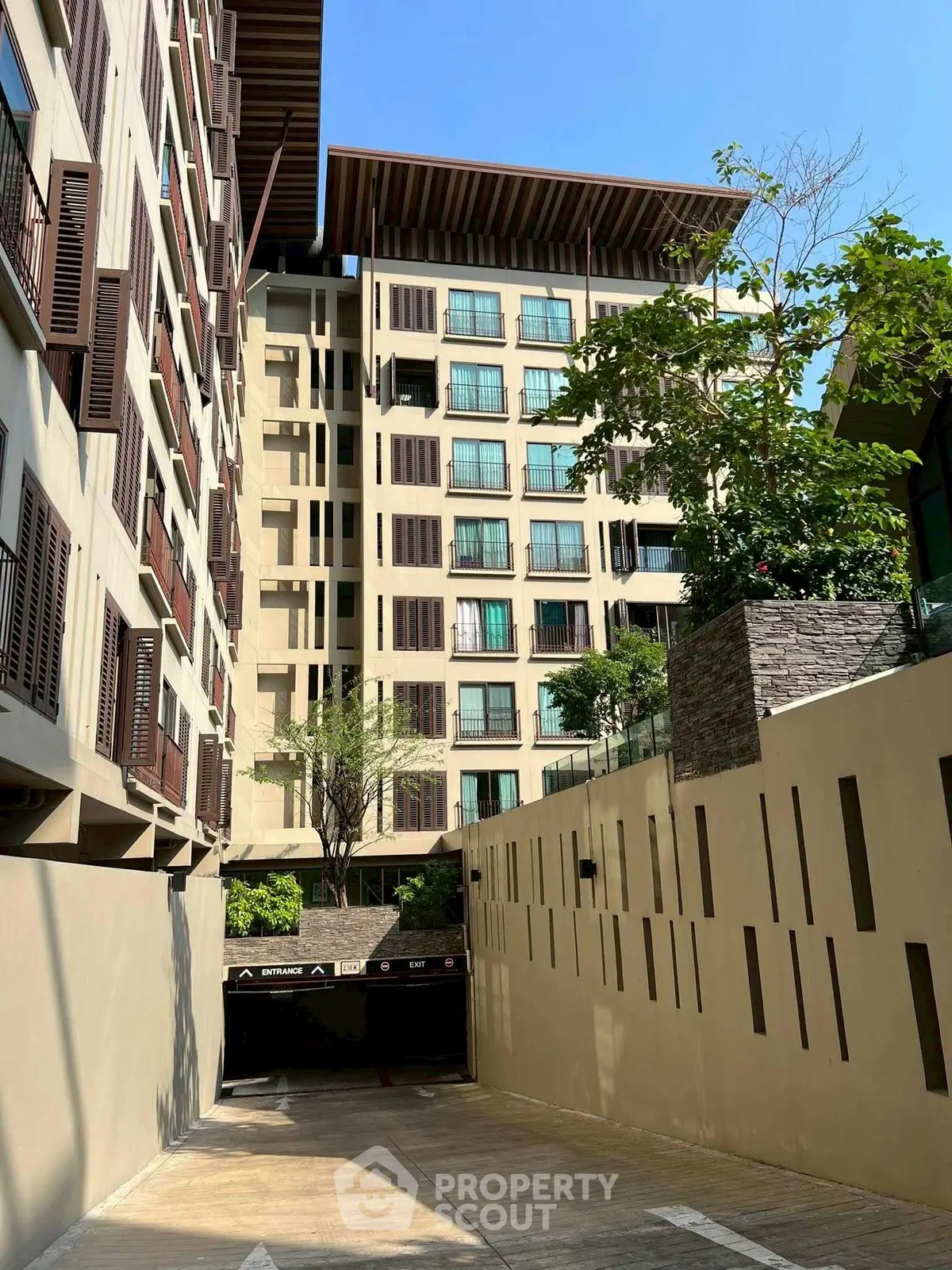 Modern residential building with lush greenery and underground parking entrance.