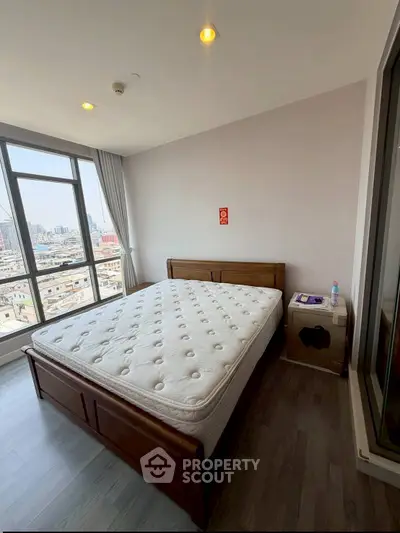 Spacious bedroom with city view and modern furnishings in high-rise apartment.