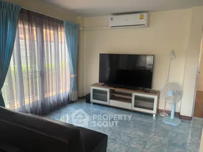 Spacious living room with large TV and natural light from balcony.