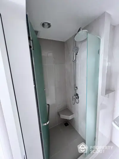 Sleek modern bathroom with glass shower enclosure and rain showerhead, featuring pristine white tiles for a clean, minimalist aesthetic.