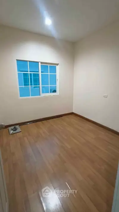 Spacious empty room with wooden flooring and large window, perfect for customization.