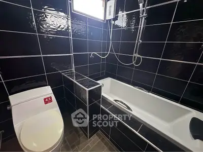 Modern bathroom with sleek black tiles and a bathtub, perfect for relaxation.