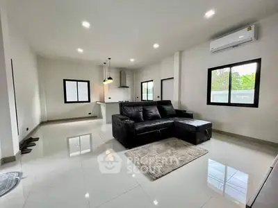 Spacious modern living room with sleek black sofa and open kitchen layout.