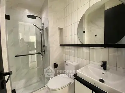 Modern bathroom with glass shower, sleek fixtures, and round mirror.