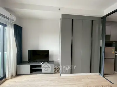 Modern living room with sleek TV stand and large wardrobe, featuring natural light from sliding glass doors.