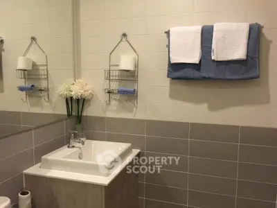 Modern bathroom with elegant sink and towel rack, featuring neutral tiles and decorative flowers.