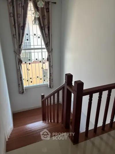 Charming wooden staircase with natural light and elegant curtains in a cozy home setting.