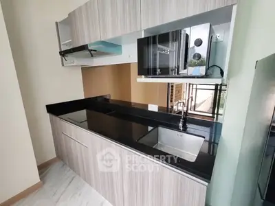 Modern kitchen with sleek cabinetry and built-in microwave, featuring a black countertop and stainless steel sink.