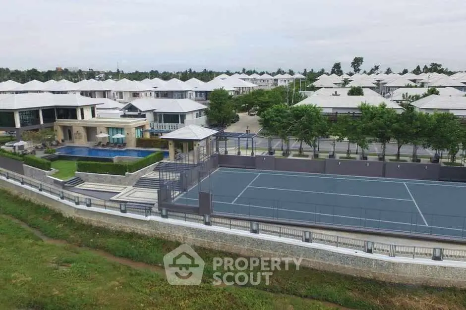 Luxurious residential complex with pool and tennis court, surrounded by lush greenery.