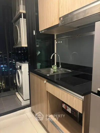 Modern kitchen with sleek cabinetry and balcony view, featuring built-in appliances and washing machine.