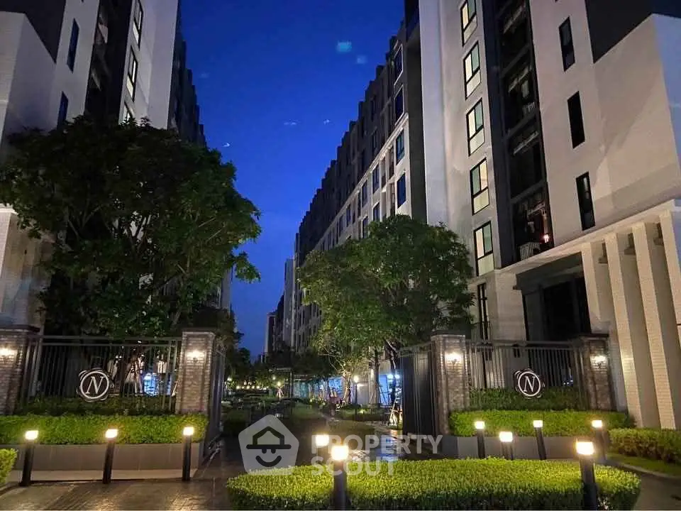 Modern apartment complex exterior with lush greenery and evening lighting.