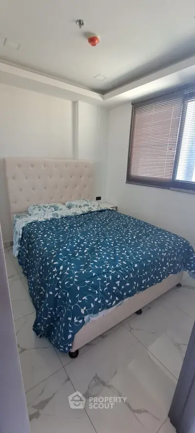 Spacious and elegantly appointed bedroom with a large comfortable bed, natural light filtering through blinds, and modern flooring, ideal for restful living.