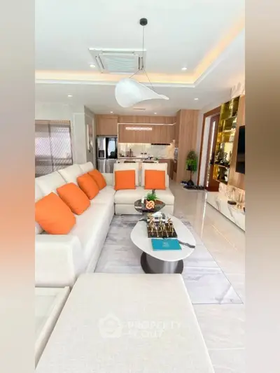 Luxurious open-plan living room with modern decor and vibrant orange accents, leading to a sleek kitchen.