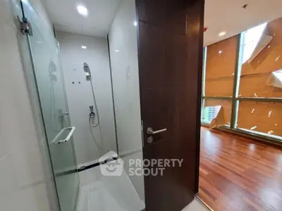 Modern bathroom with glass shower and adjacent room with wooden flooring.