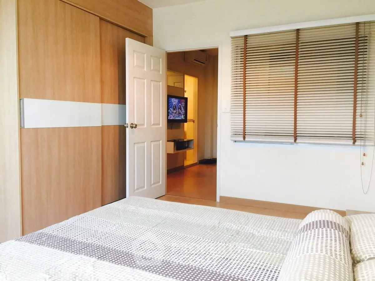 Cozy bedroom with modern decor and wooden accents, featuring a view into a living area with a TV.