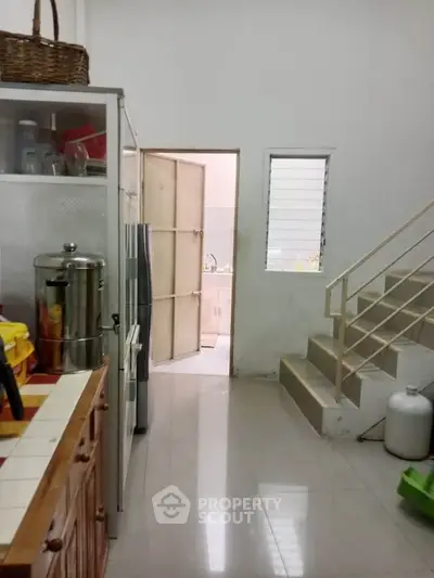 Cozy kitchen with tiled countertops and staircase, featuring a sleek fridge and ample storage space.