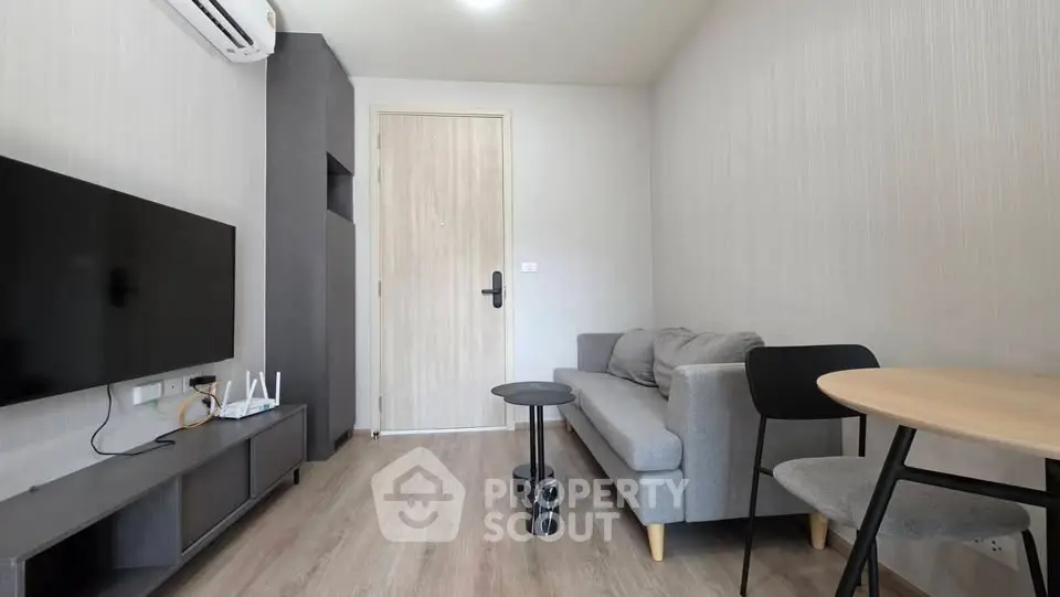 Modern living room with sleek furniture and minimalist design, featuring a wall-mounted TV and air conditioning.