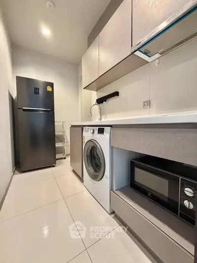Modern kitchen with sleek appliances including fridge, washing machine, and microwave in a compact layout.