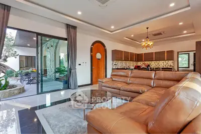 Luxurious open-plan living room with leather sofa and modern kitchen, featuring elegant lighting and outdoor view.