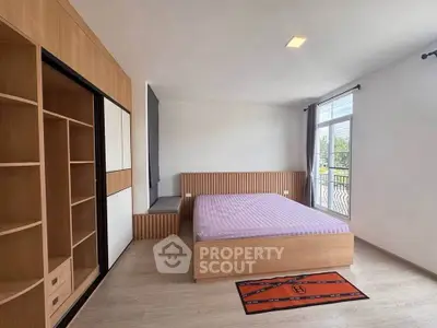 Spacious modern bedroom with large window and built-in wooden wardrobe.