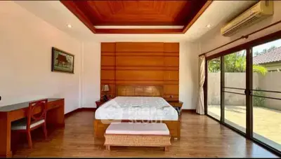Spacious bedroom with wooden accents and large windows opening to a garden view.