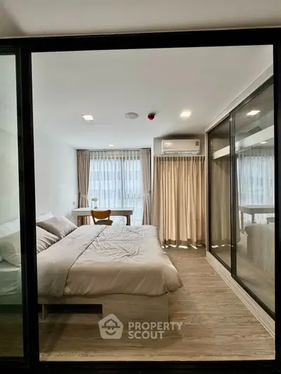 Modern bedroom with large windows and natural light, featuring a cozy bed and work desk.