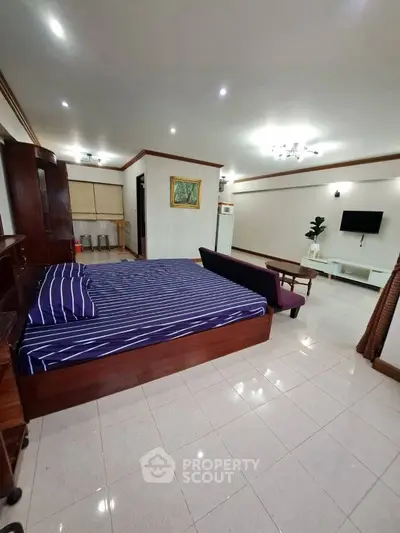 Spacious bedroom with modern furnishings and tiled flooring, featuring a cozy bed and wall-mounted TV.