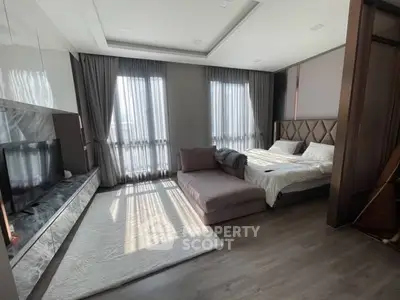 Luxurious bedroom with elegant decor and natural light, featuring a cozy bed and modern entertainment setup.