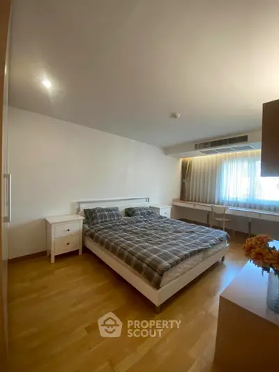 Spacious bedroom with wooden flooring and natural light, featuring a cozy bed and modern furnishings.