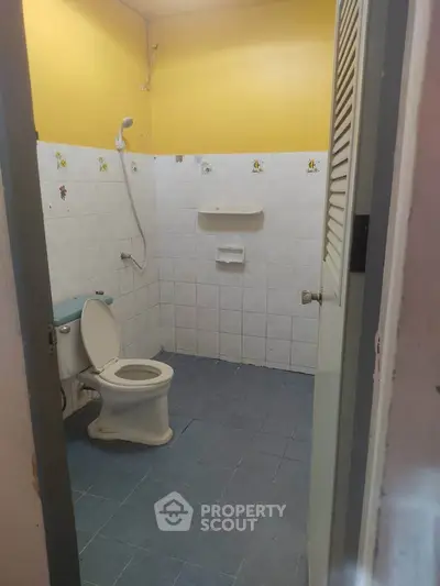 Cozy bathroom with yellow walls and blue tile flooring, featuring a toilet and shower area.