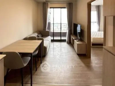 Modern open-plan living room with cozy seating and natural light, leading to a bedroom with balcony access.