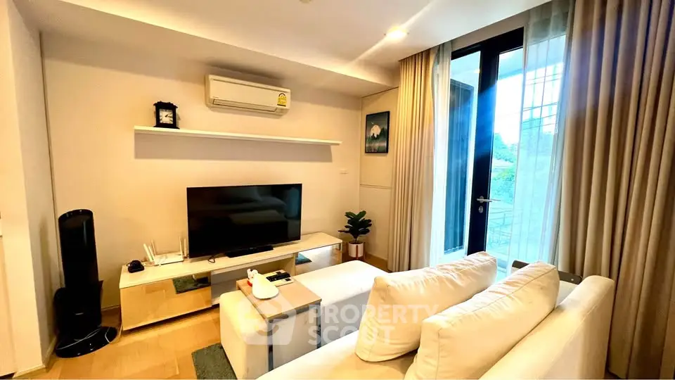 Modern living room with cozy seating and large TV, featuring natural light and stylish decor.