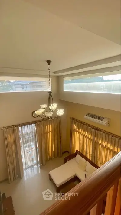 Spacious living room with high ceiling and elegant lighting, featuring large windows and cozy seating area.