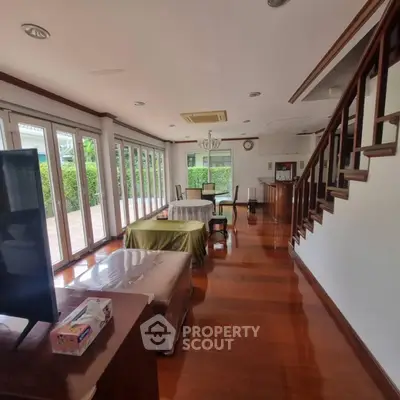 Spacious living room with wooden flooring and large windows opening to a garden view.