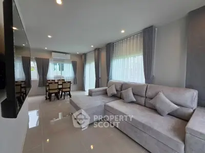 Spacious modern living room with elegant gray sofa and dining area, featuring large windows and sleek tile flooring.
