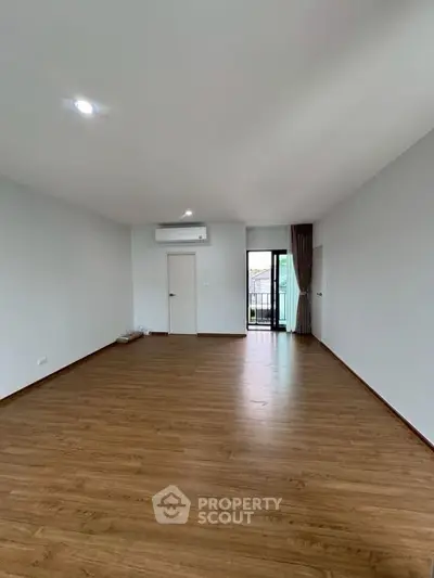 Spacious empty living room with wooden flooring and balcony access, perfect for customization.