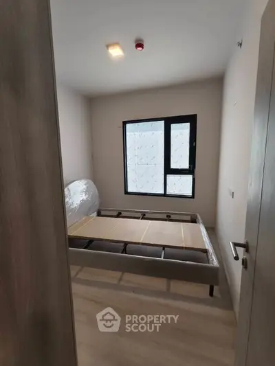 Modern bedroom with large window and bed frame, showcasing minimalist design and natural light.