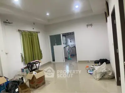Spacious living room with tiled flooring and green curtains, adjacent to a kitchen area.