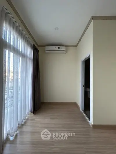 Spacious and well-lit empty room with large windows draped in sheer curtains, complemented by elegant dark curtains, and a modern air conditioning unit, ready for personalization.