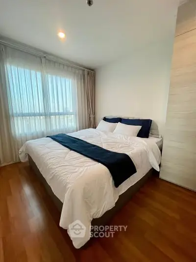 Cozy bedroom with large window and elegant wooden flooring in modern apartment.