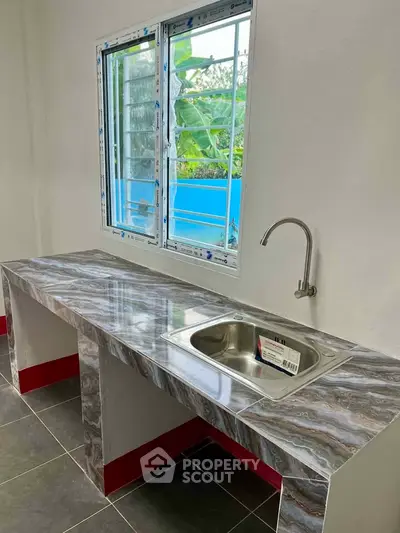 Modern kitchen with sleek marble countertop and stainless steel sink, featuring a large window with garden view.