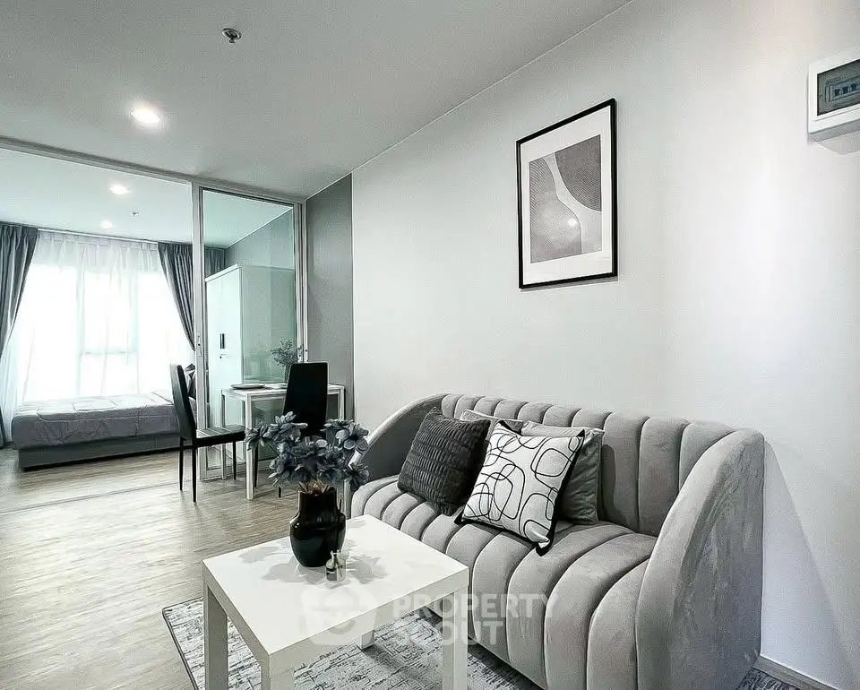 Modern living room with stylish sofa and elegant decor, adjacent to a bright bedroom with large windows.