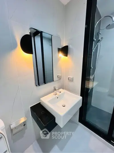 Modern bathroom with sleek sink and illuminated mirror, featuring a glass shower enclosure.