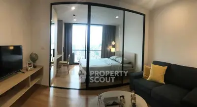 Modern living room with glass partition leading to a cozy bedroom, featuring stylish decor and natural light.