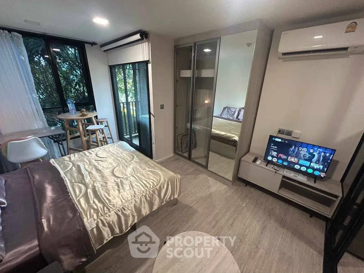 Modern bedroom with mirrored wardrobe, TV, and small dining area near window.