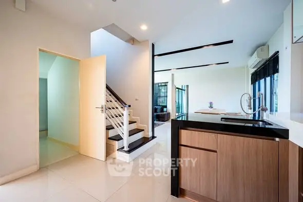 Modern open-plan kitchen with sleek design and staircase leading to upper floor